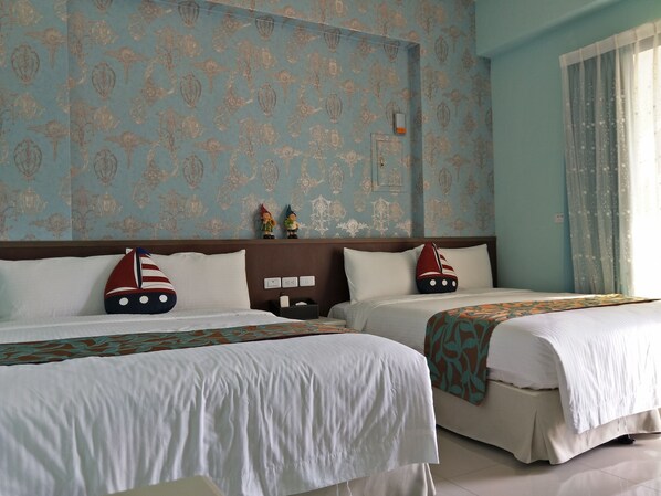 A hotel room with two beds, each with a sailboat pillow. The room has a patterned wallpaper and a window with curtains.