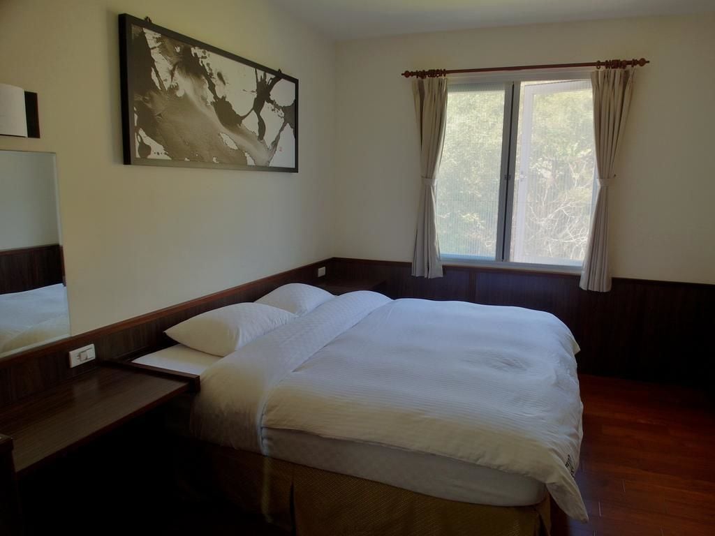 A hotel room with a large bed, a bedside table, a mirror, and a window with curtains.