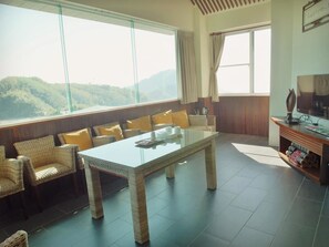 A spacious room with a large glass table, wicker furniture, and a view of the mountains. - Tea Cloud Guest House (Alishan)