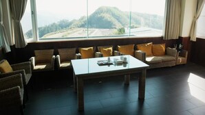 A room with wicker furniture, a glass-top table, and a large window offering a view of a hilly landscape. - Tea Cloud Guest House (Alishan)