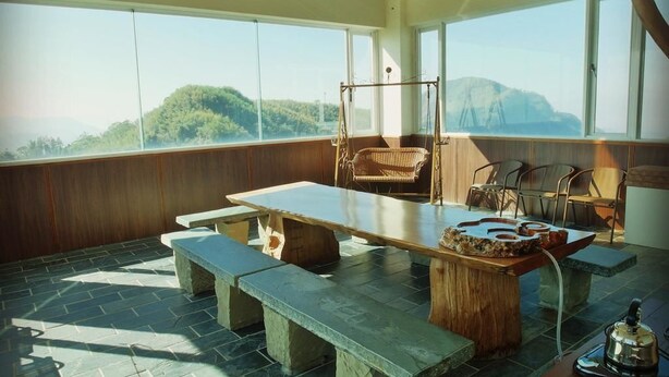 A room with a large table, benches, and a hanging chair. There are large windows with a view of a forested hill. - Tea Cloud Guest House (Alishan)