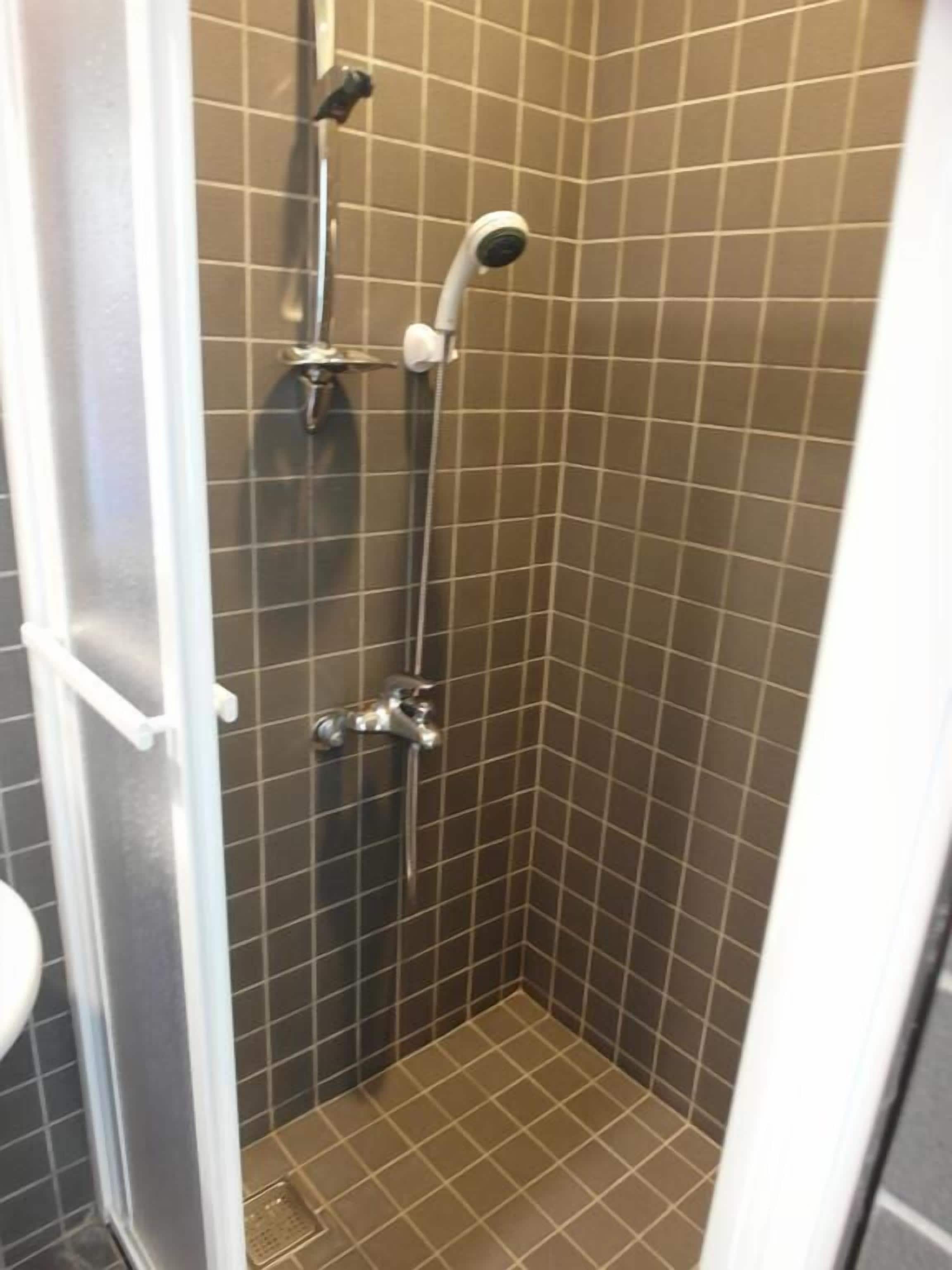A small, tiled shower stall with a handheld showerhead and a wall-mounted faucet.