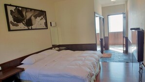 A hotel room with a large bed, a flat-screen TV, a painting on the wall, and a view of the outdoors through an open door. - Tea Cloud Guest House (Alishan)