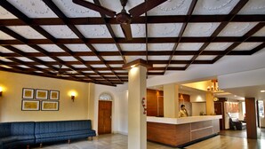 A reception area with a wooden ceiling, a reception desk, a blue sofa, and framed pictures on the wall. - Hotel Aida (Kottayam)