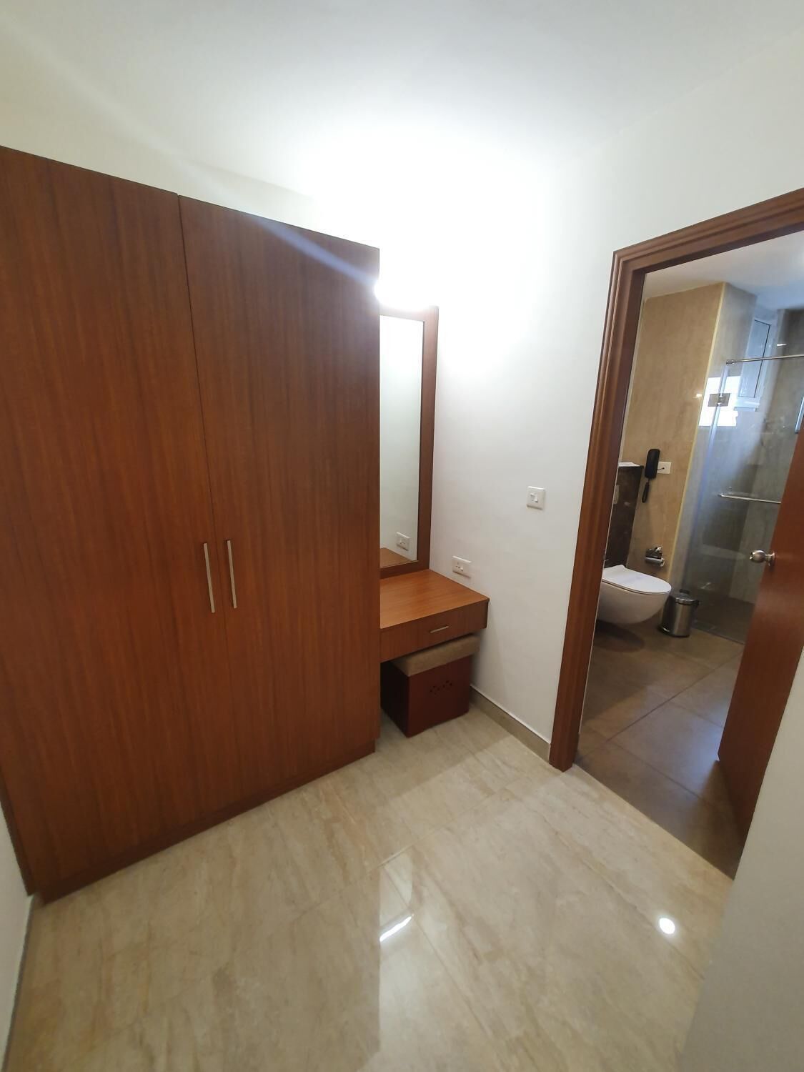 A bedroom with a wooden wardrobe, a bedside table, and a mirror.