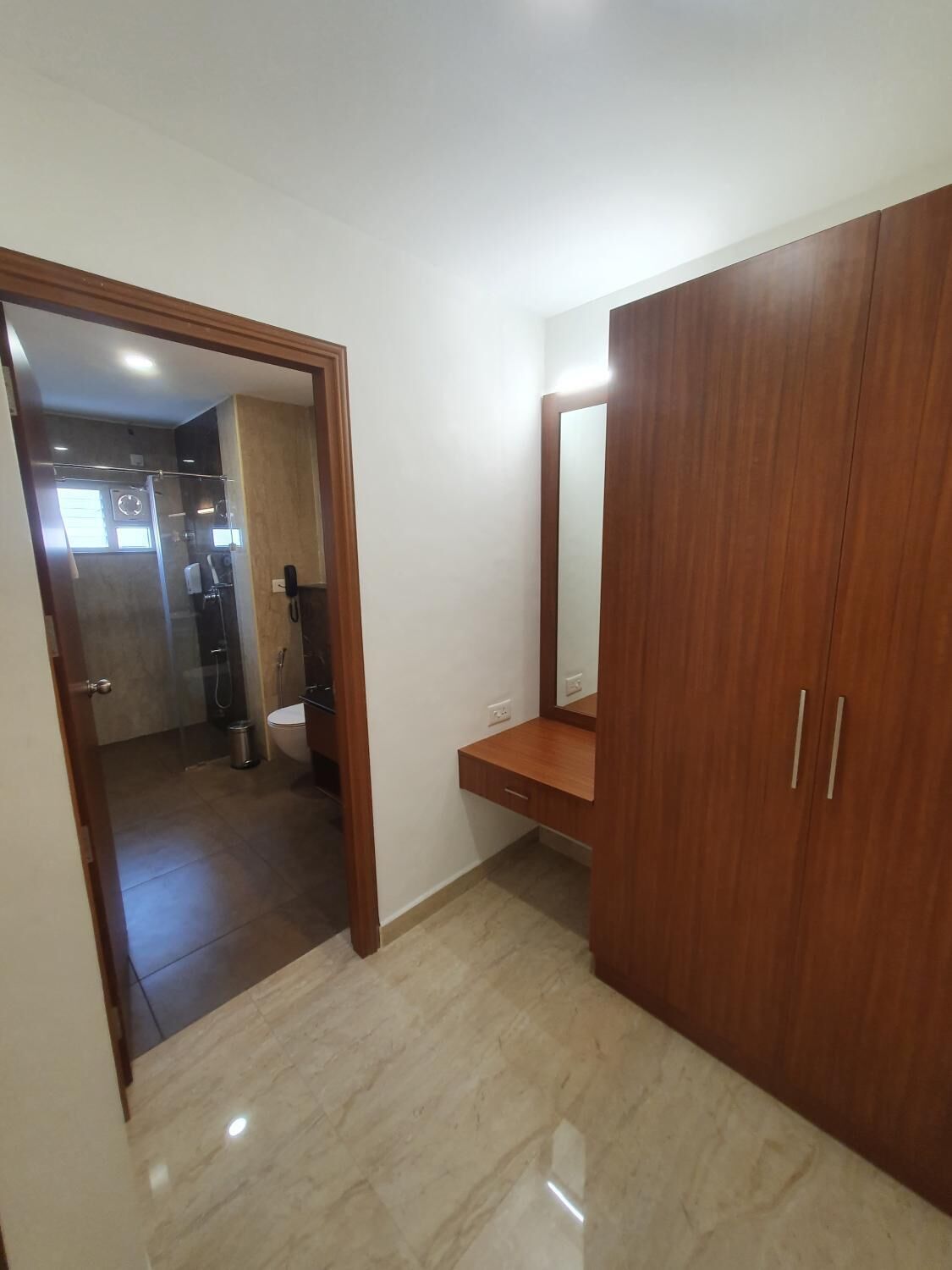 Una habitación con un armario de madera, un espejo y un baño visible a través de una puerta abierta.