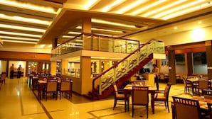 A hotel lobby with a central staircase, multiple dining areas, and a reception desk. - Hotel Aida (Kottayam)