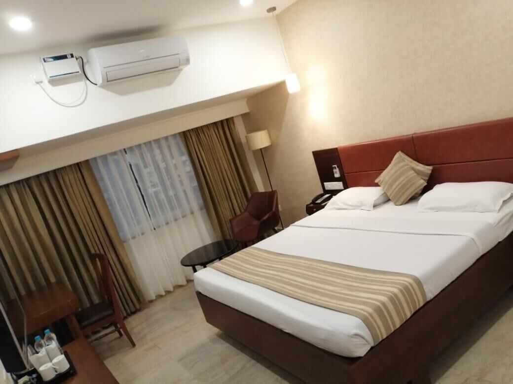 Habitación de hotel con una cama grande, un escritorio con silla, un equipo de aire acondicionado y cortinas.