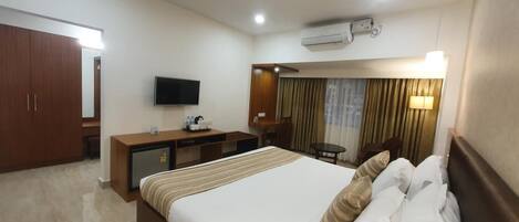 A hotel room with a large bed, a desk, a television, and an air conditioning unit.