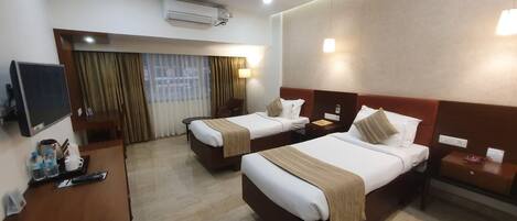 A hotel room with two beds, a desk, a TV, and an air conditioning unit.