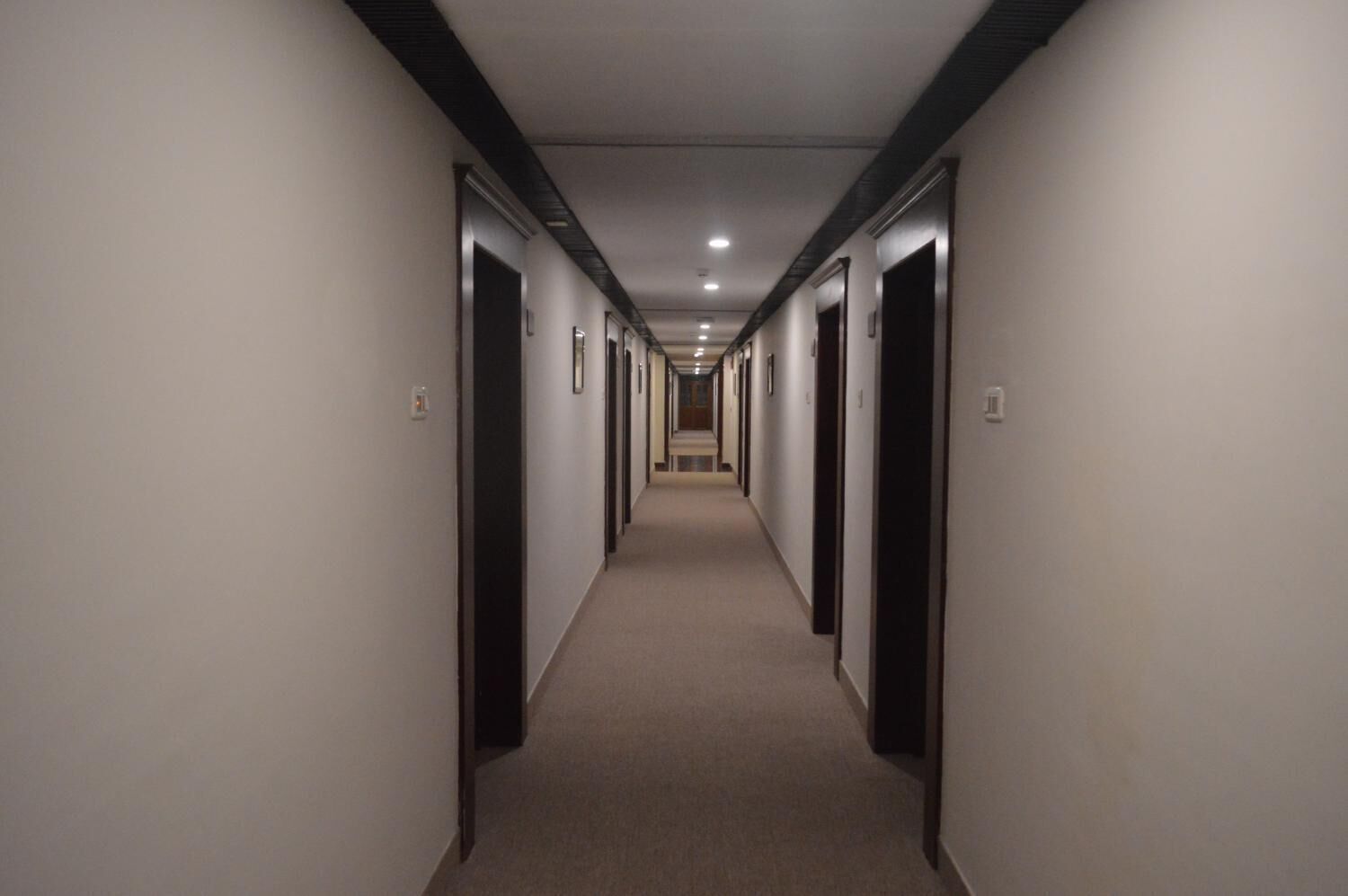 Corredor longo e estreito de hotel, com portas de ambos os lados e piso coberto por carpete.