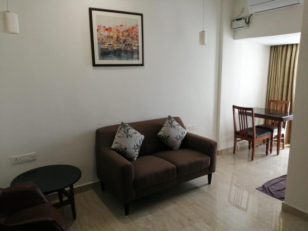 A living room with a brown sofa, two patterned pillows, a small round table, and a framed painting on the wall.