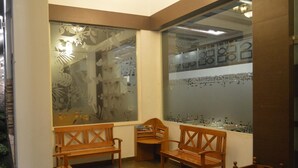 A room with wooden benches, a trash bin, and a large window with decorative glass panels. - Hotel Aida (Kottayam)