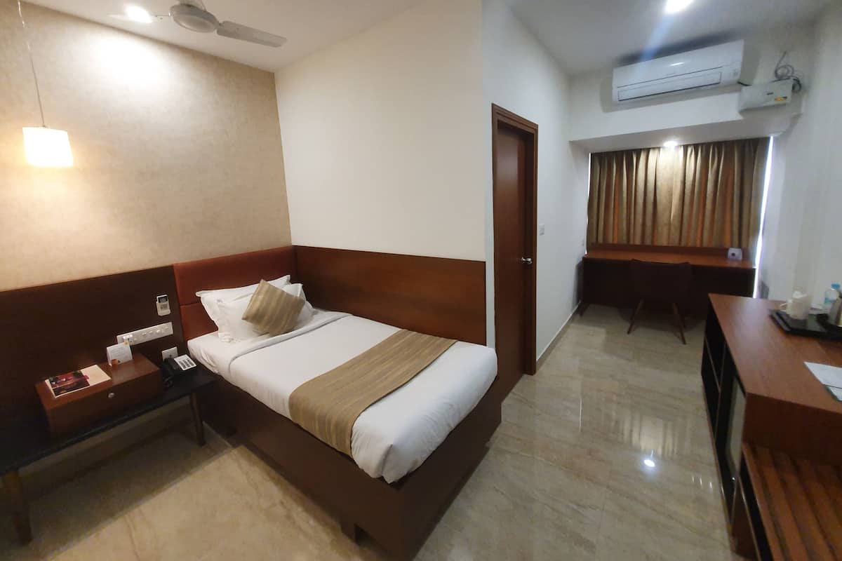 Habitación de hotel con cama, mesita de noche, escritorio, silla y equipo de aire acondicionado.