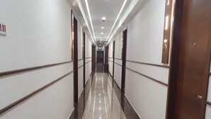 A long, narrow hallway with a shiny, reflective floor and white walls. - Hotel Aida (Kottayam)