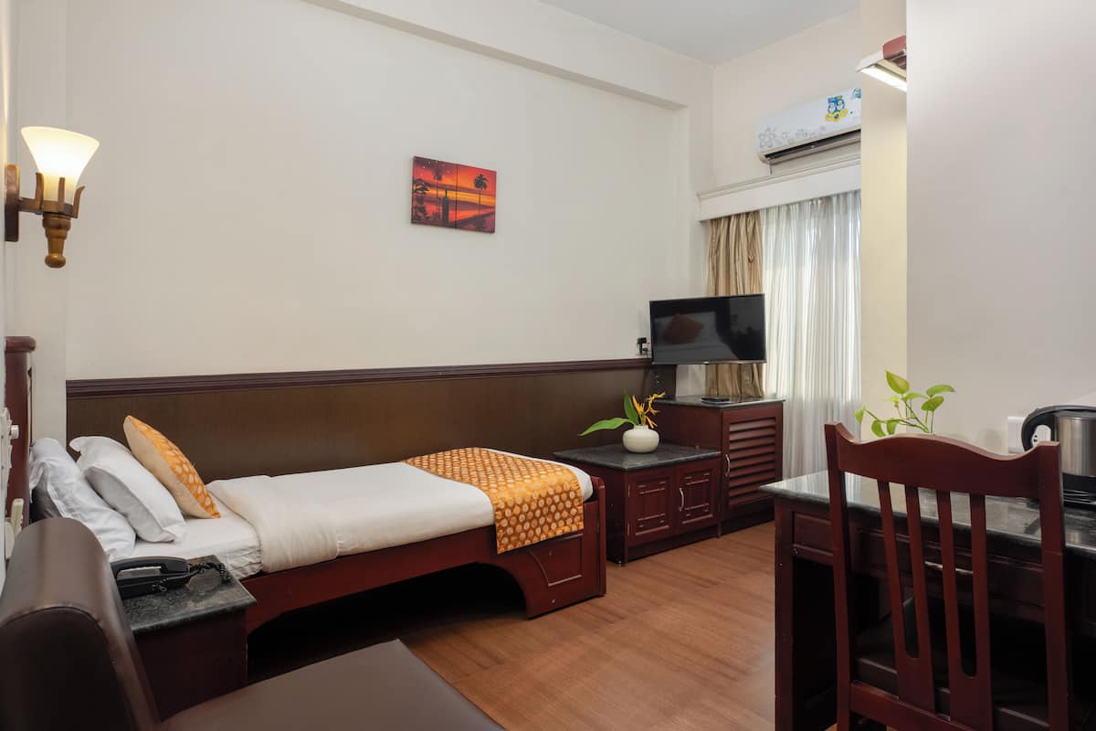 Una habitación de hotel con cama, escritorio, silla, televisor y aire acondicionado instalado en la pared.