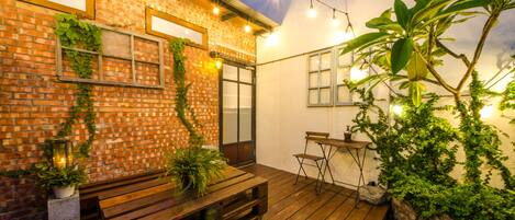 Un patio con terraza de madera, pared de ladrillo y luces colgantes.