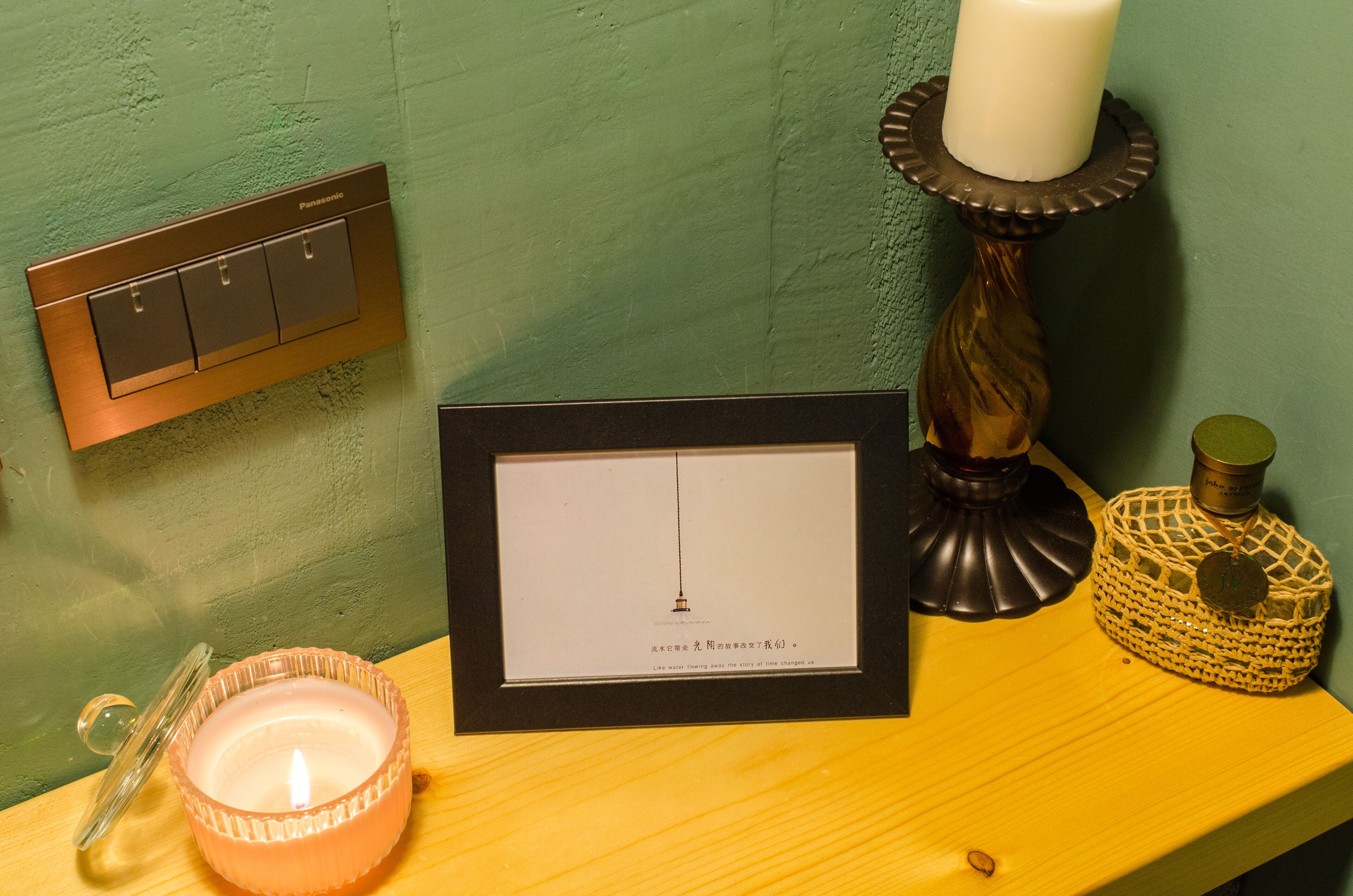 A framed certificate, a candle, a decorative candle holder, and a switch on a wooden shelf.