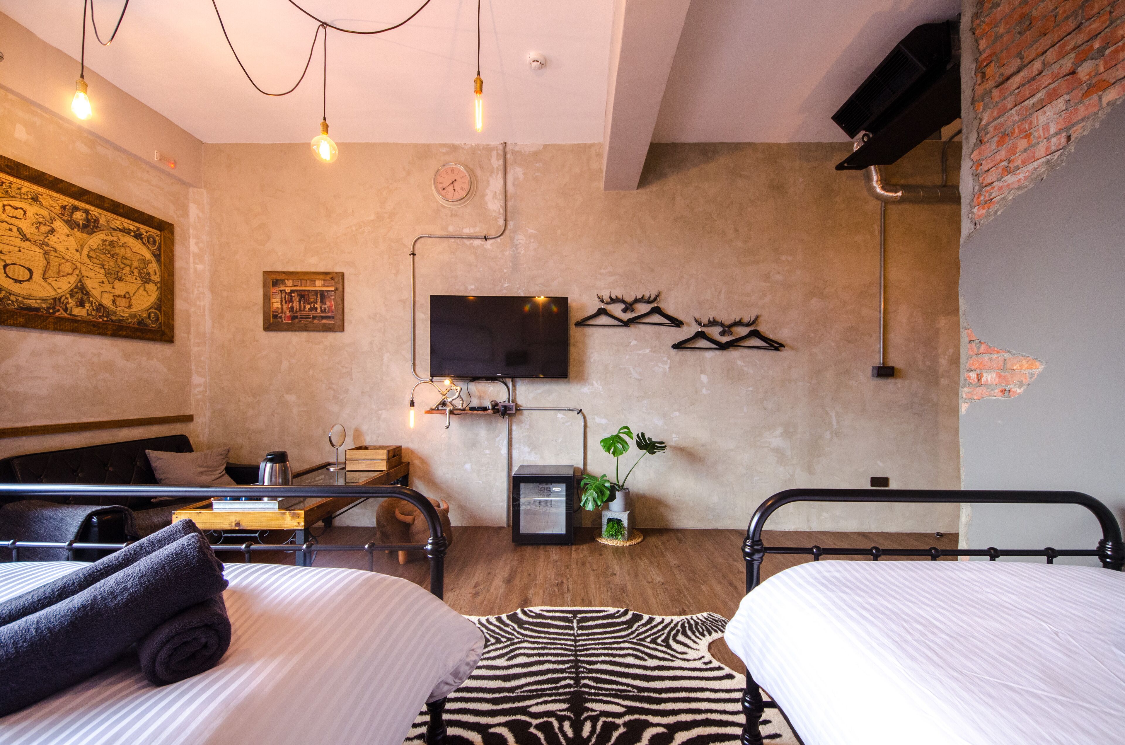 A hotel room with two beds, a flat-screen TV, a clock, and a plant.