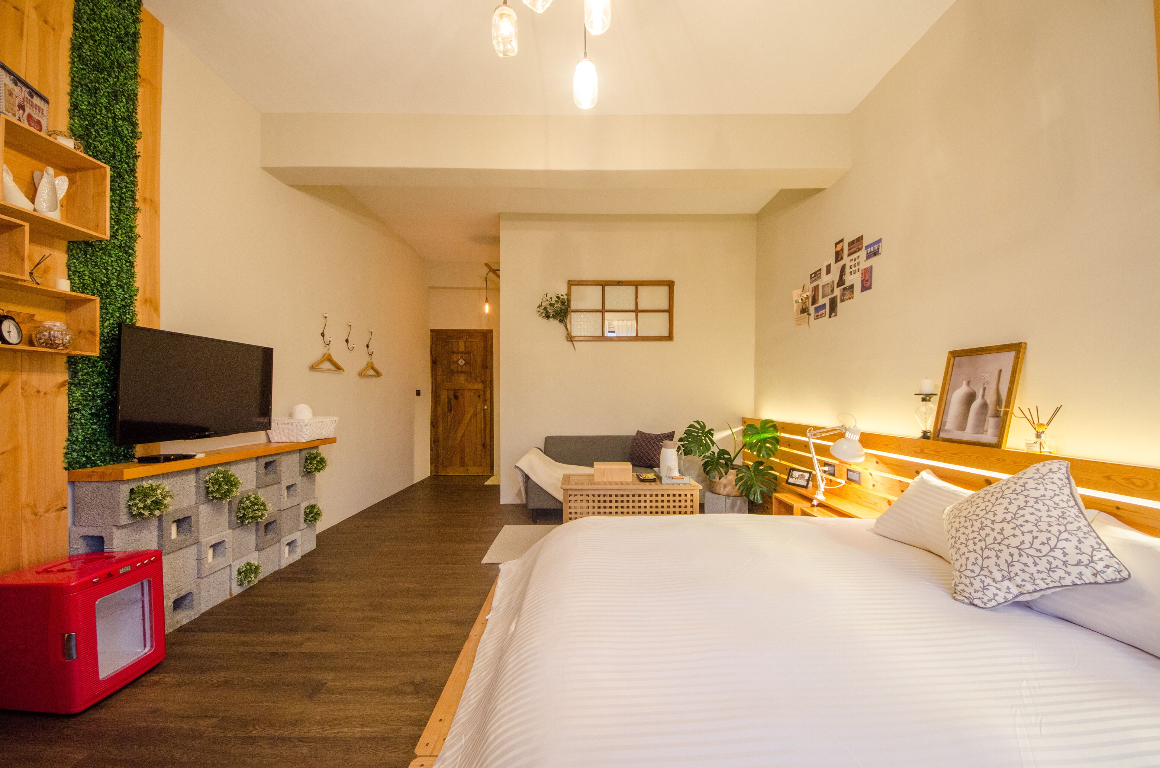 Una habitación de hotel moderna con una cama grande, un televisor en un estante de madera, un escritorio pequeño y una pared verde.