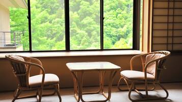 Una habitación con dos sillas de mimbre y una mesa pequeña, un ventanal con vistas a un bosque frondoso.