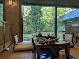 A traditional Japanese-style room with tatami flooring, a low table with tea utensils, and a view of a lush garden.