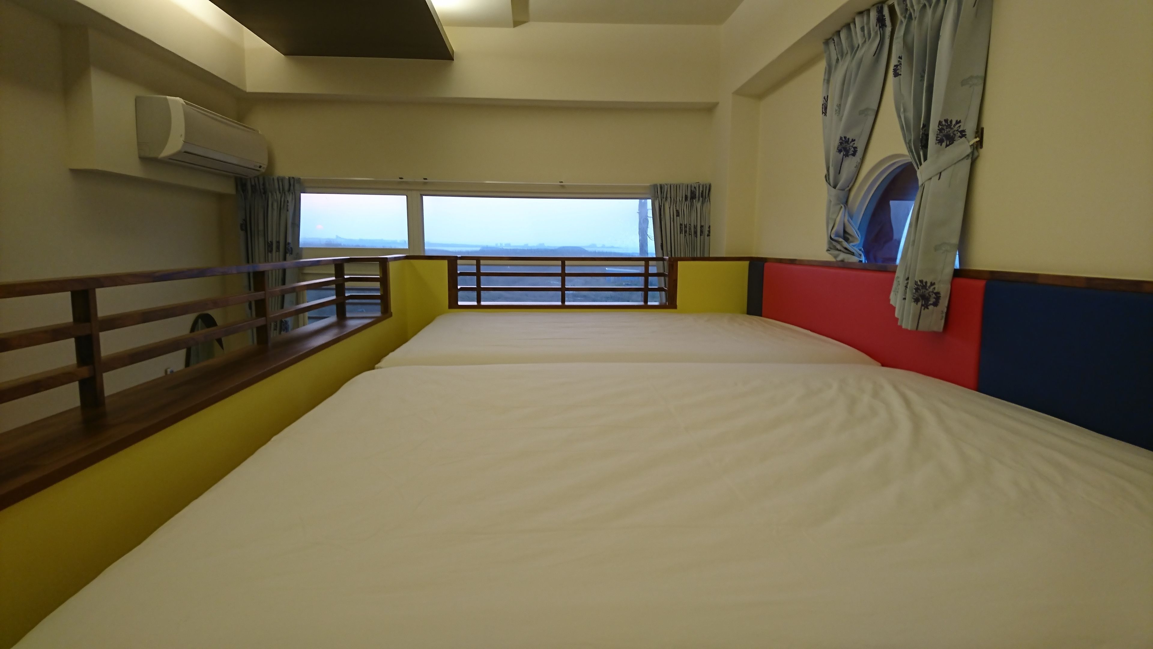 Habitación de hotel con una cama grande, una ventana con vistas, barandilla de madera y unidad de aire acondicionado.