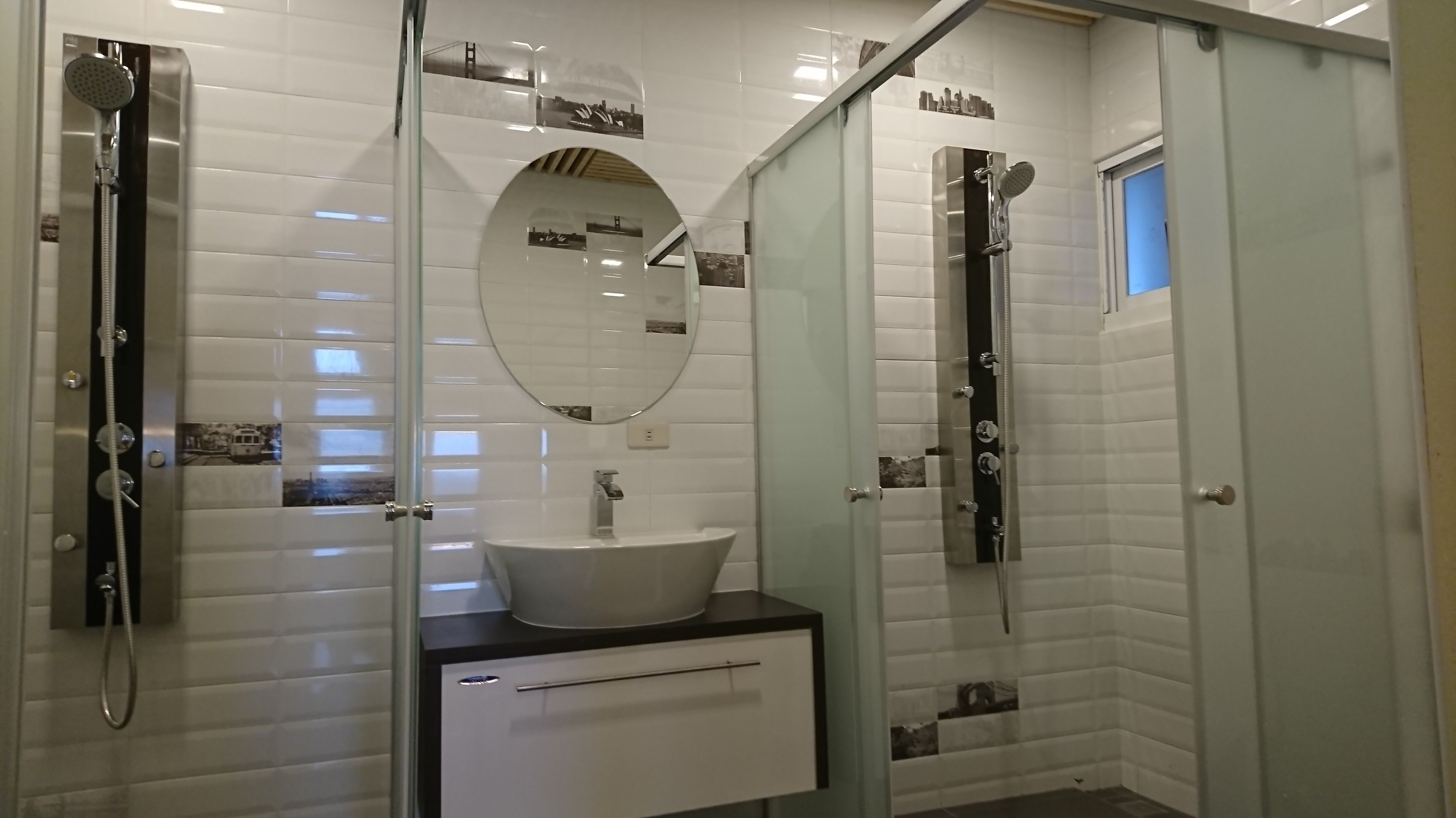 A modern bathroom with white subway tiles, a round mirror, a white sink, and a glass-enclosed shower area.