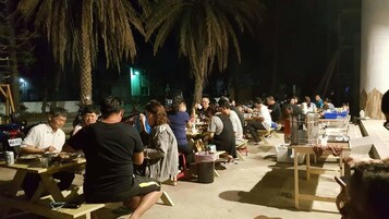 Un espacio exterior para comer con mesas y sillas, palmeras y un escenario al fondo.