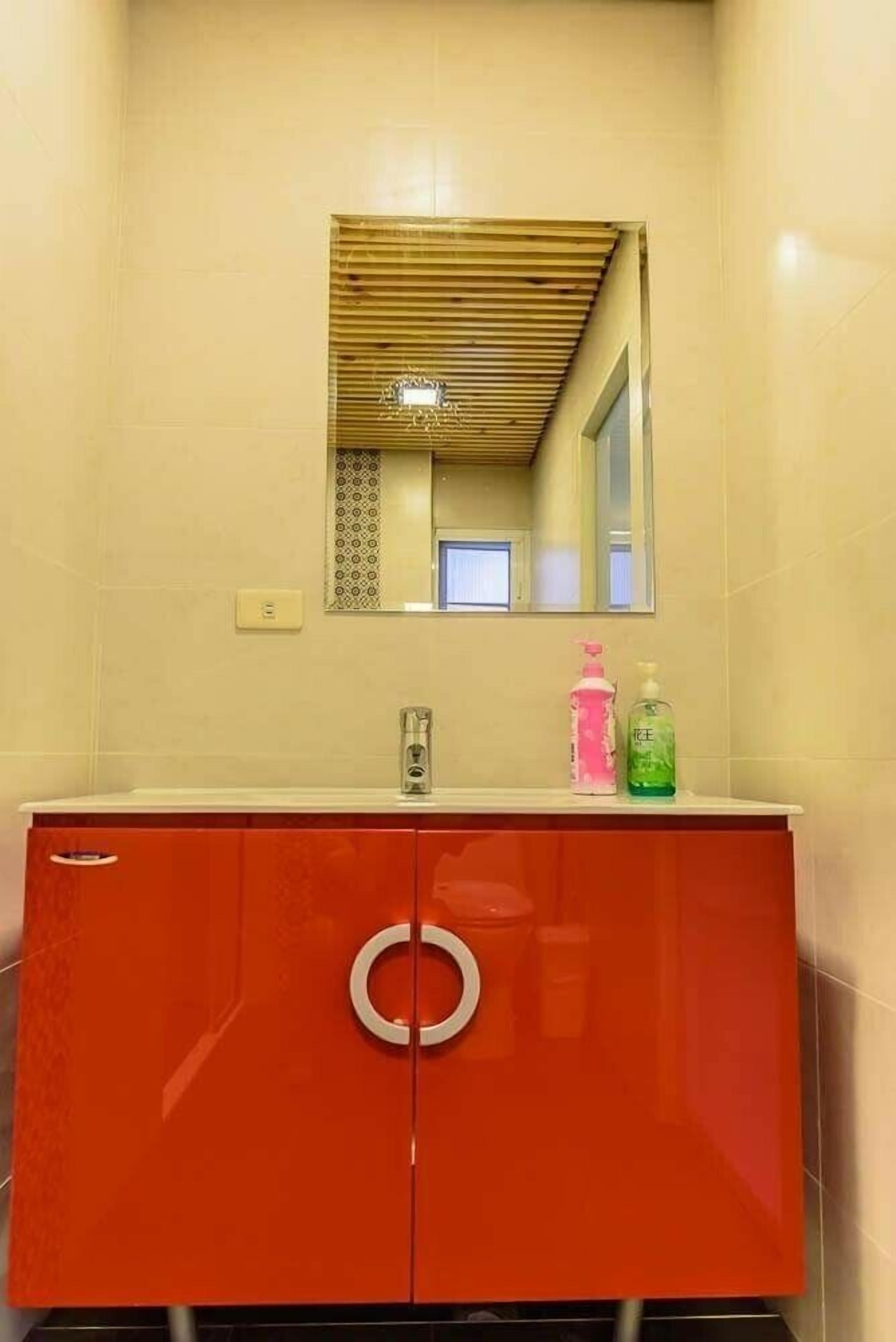 A bathroom with a red cabinet, a mirror, and two bottles of liquid soap.