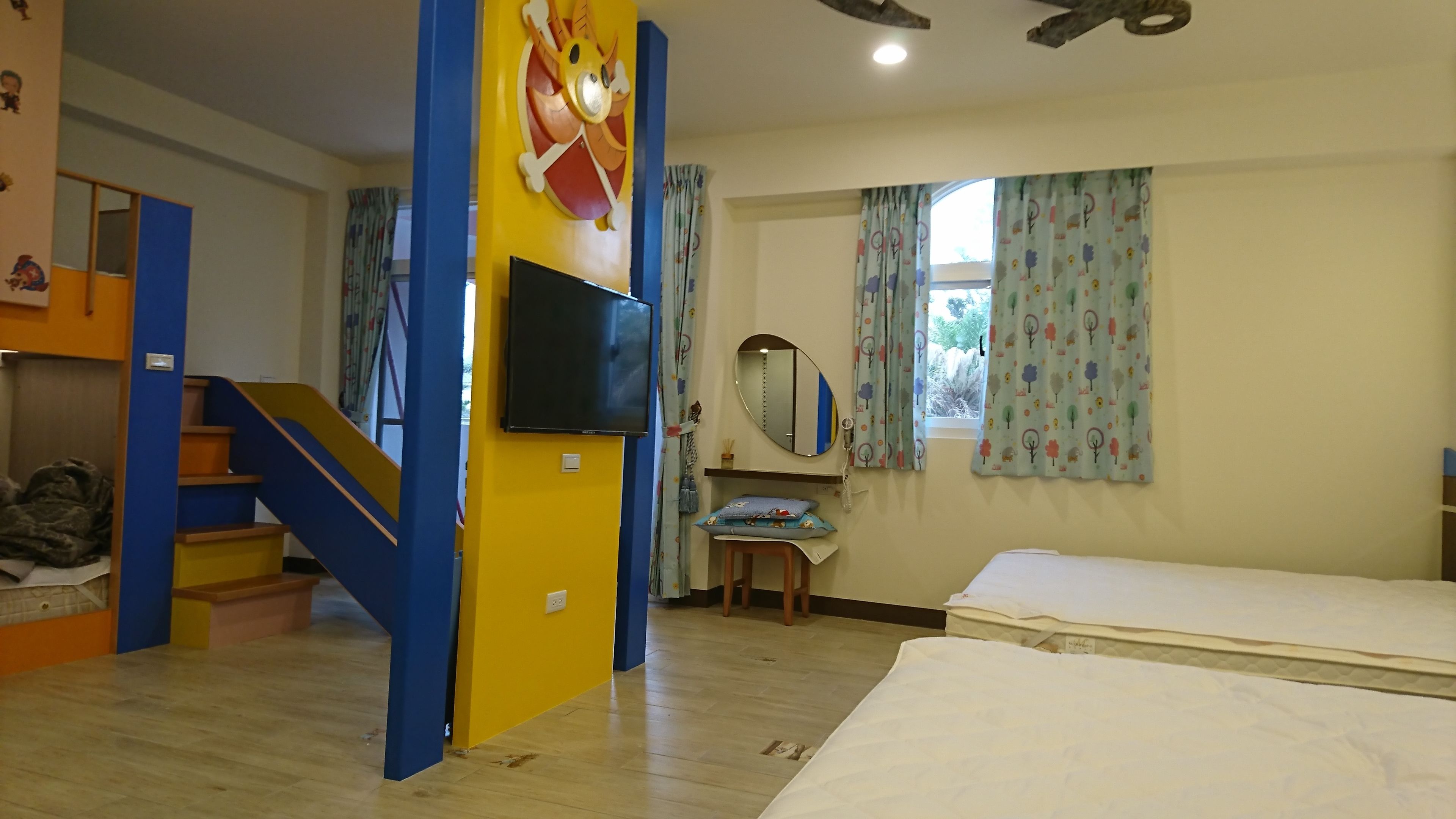 A room with a bunk bed, a desk with a chair, a television, a window with curtains, and a mirror on the wall.