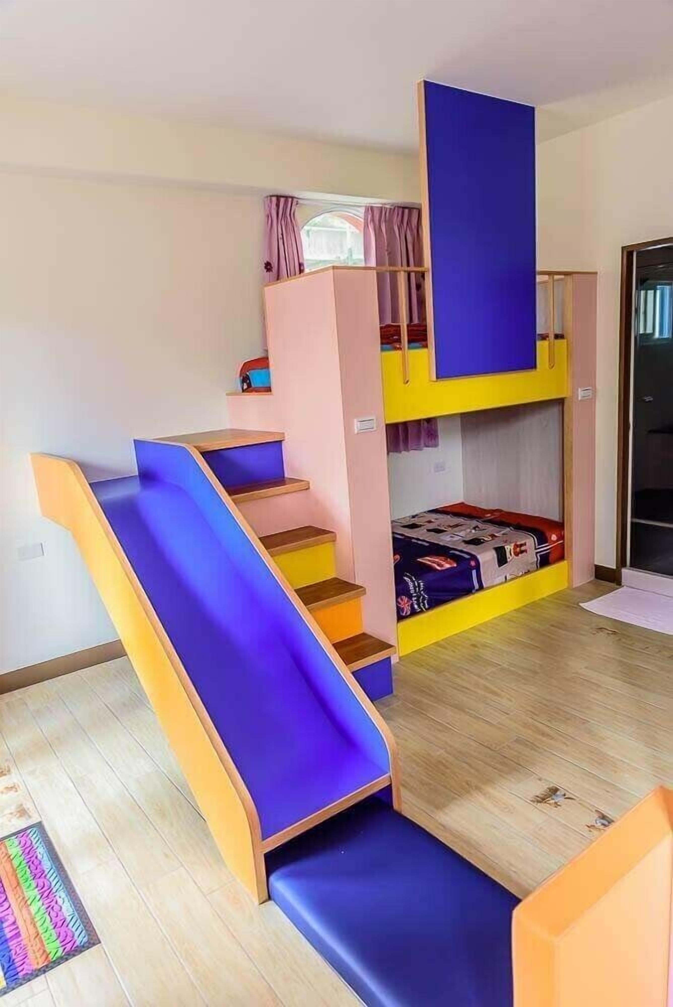 A bunk bed room with a slide, pink and yellow walls, and a window with curtains.