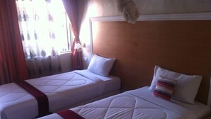Ein Hotelzimmer mit zwei Einzelbetten, jeweils mit roter Bettdecke, weißen Kissen und einem hölzernen Kopfteil.