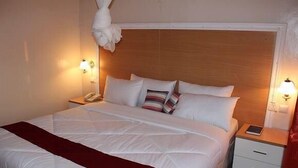 Ein Hotelzimmer mit einem großen Bett, zwei Nachttischen, einem Holzkopfstück und zwei Wandlampen.