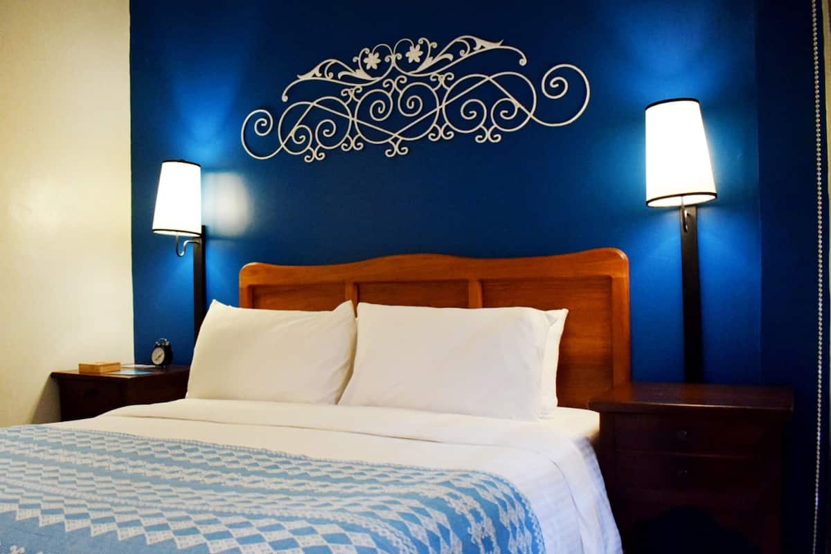 A hotel room with a wooden headboard, two bedside lamps, a clock, and a patterned bedspread.