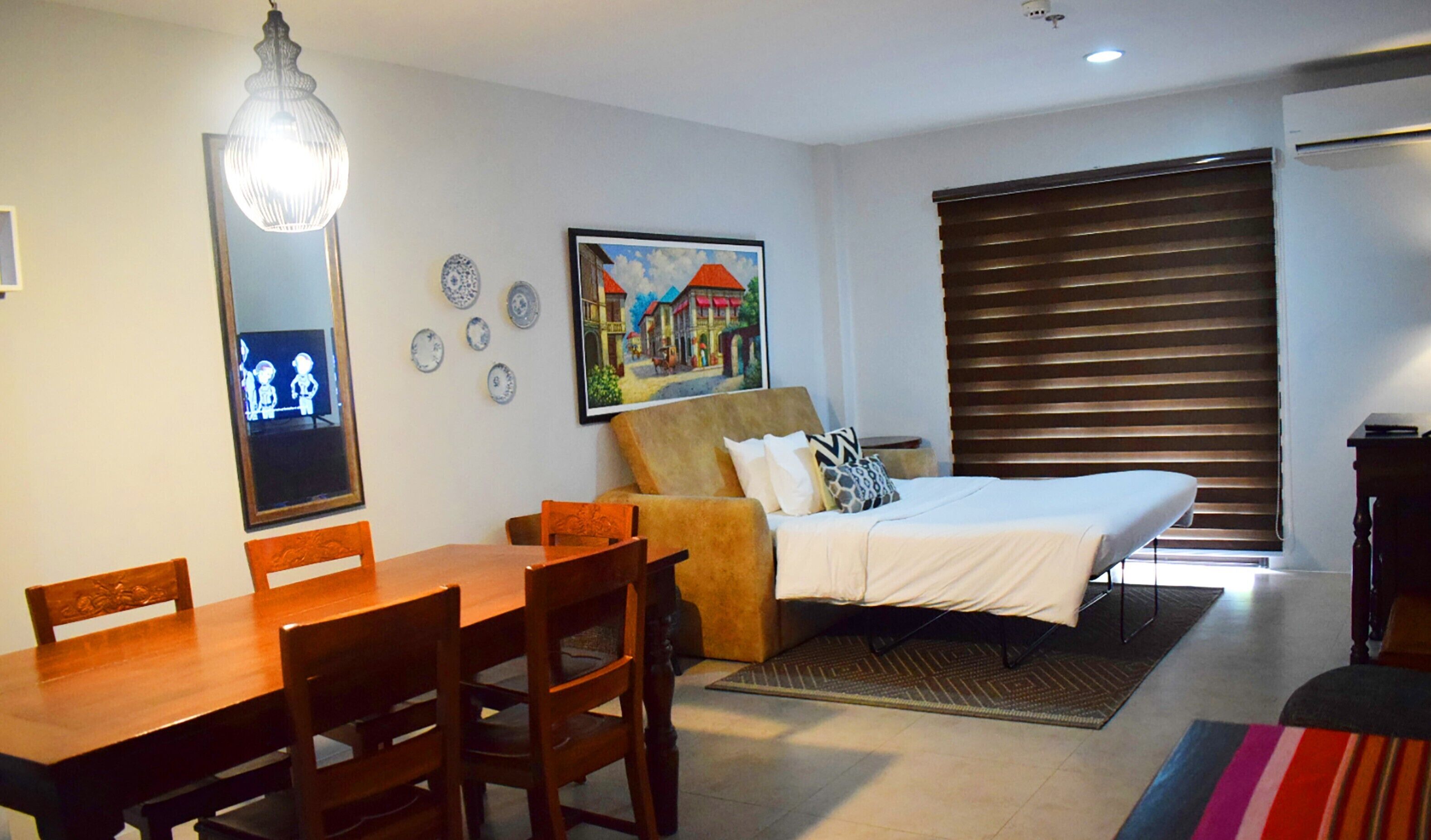 Un dormitorio con cama, sofá, mesa de comedor con sillas, espejo y un cuadro en la pared.