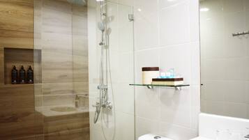 Un baño moderno con ducha de vidrio, tocador de madera y estante de vidrio con artículos de aseo.