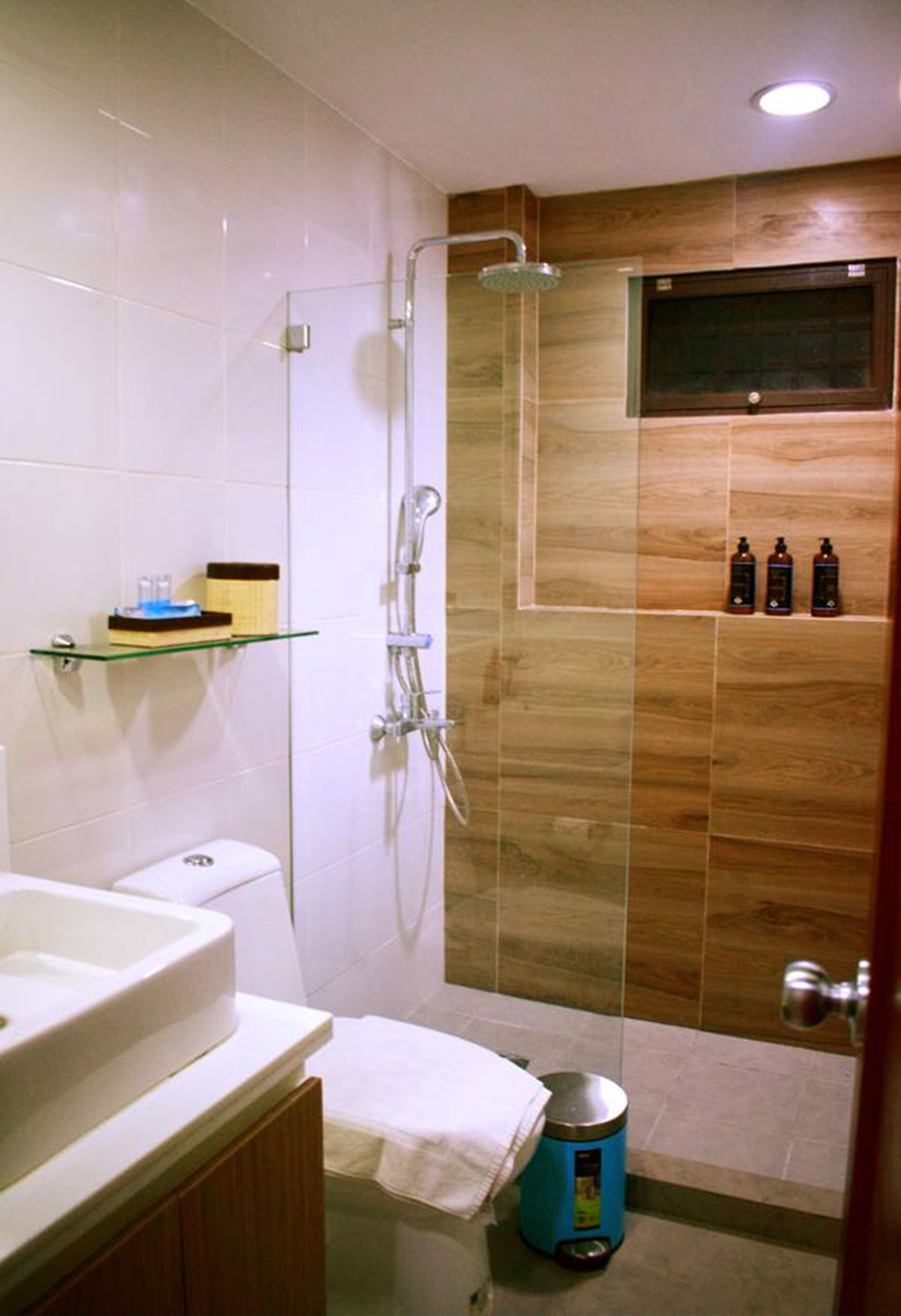A bathroom with a glass-enclosed shower, a toilet, a sink, and a shelf with toiletries.