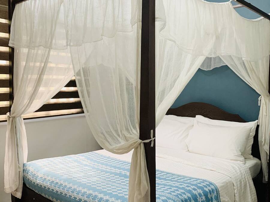 A four-poster bed with white net curtains, a blue patterned bedspread, and white pillows.
