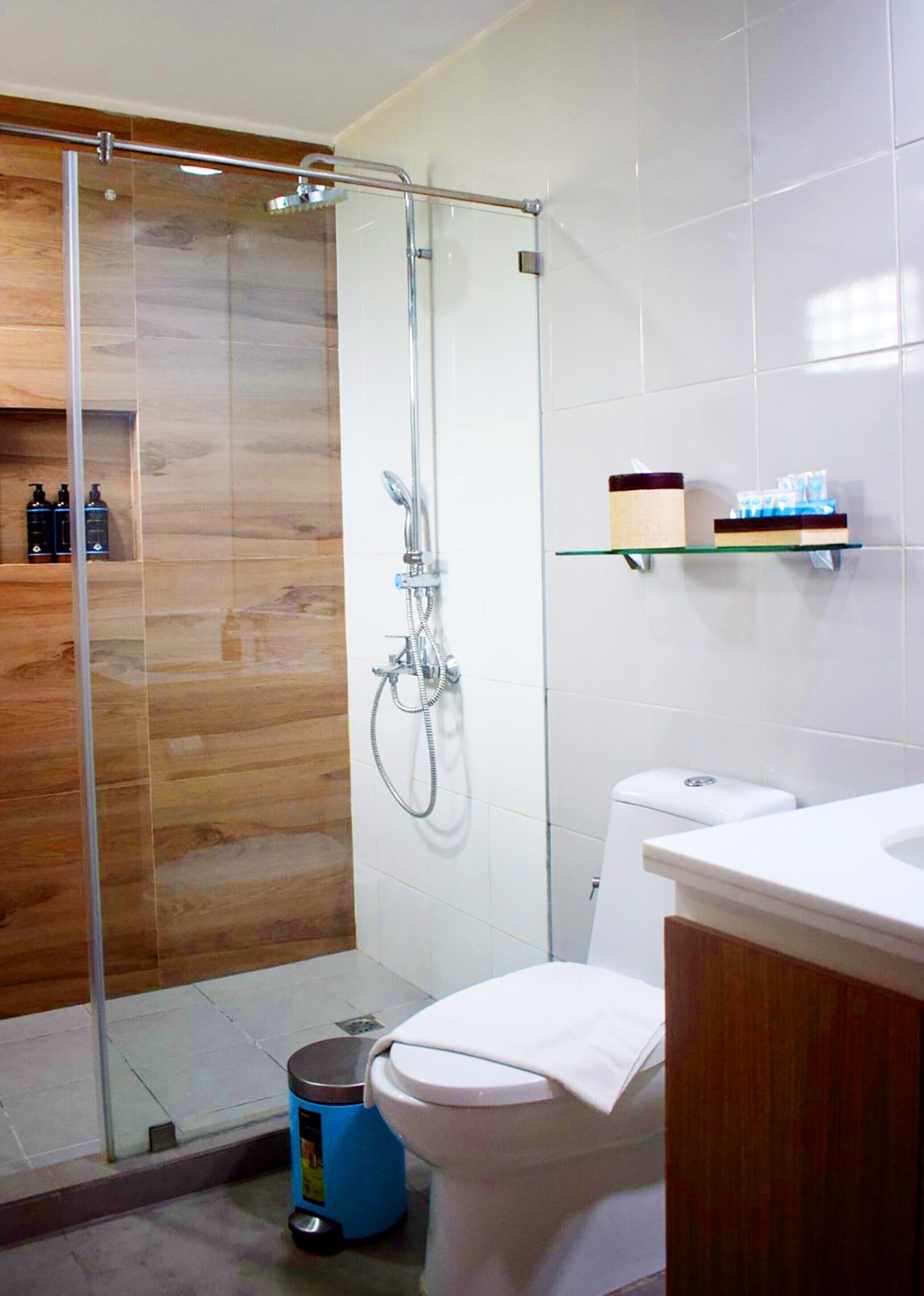 Un baño moderno con cabina de ducha de vidrio, inodoro y lavabo con tocador de madera.