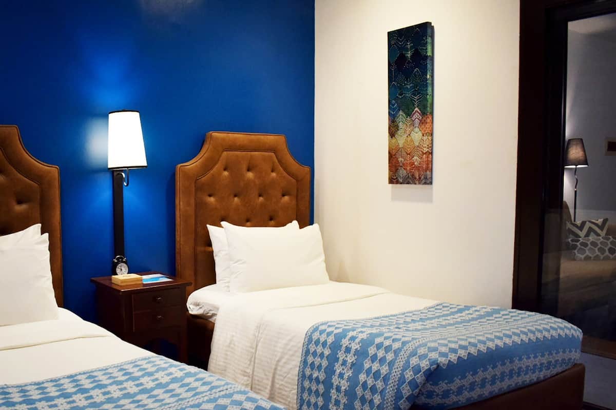 A hotel room with two beds, a nightstand with a lamp, and a painting on the wall.