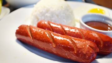 Une assiette avec deux saucisses, une portion de riz et un petit bol de sauce.