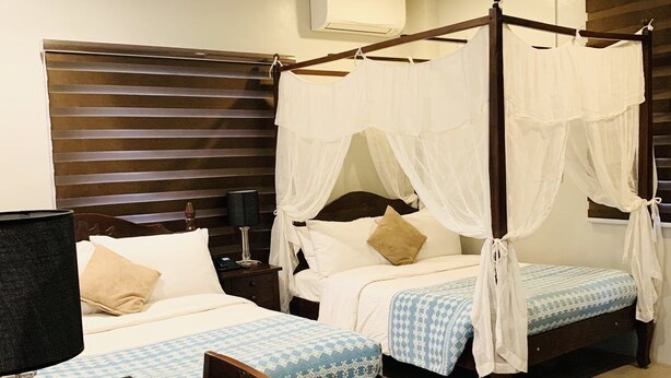 A hotel room with two beds, a wooden headboard, a bedside table with a lamp, and a magazine on the table. - Paradores de Vigan (Vigan)