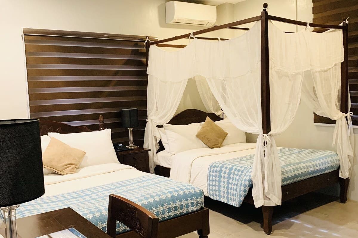 A hotel room with two beds, a wooden headboard, a bedside table with a lamp, and a magazine on the table.