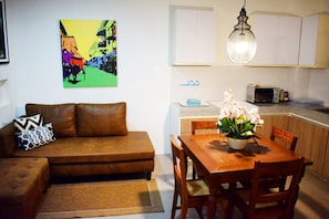 A living room with a brown sofa, a dining table with chairs, a vase of flowers, and a kitchen area with cabinets and a microwave.