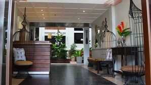 A spacious lobby with a high ceiling, a central seating area with a cushioned bench, and a reception desk. - Paradores de Vigan (Vigan)