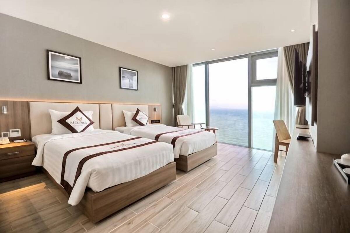 A hotel room with two beds, a large window, a desk, and a chair.