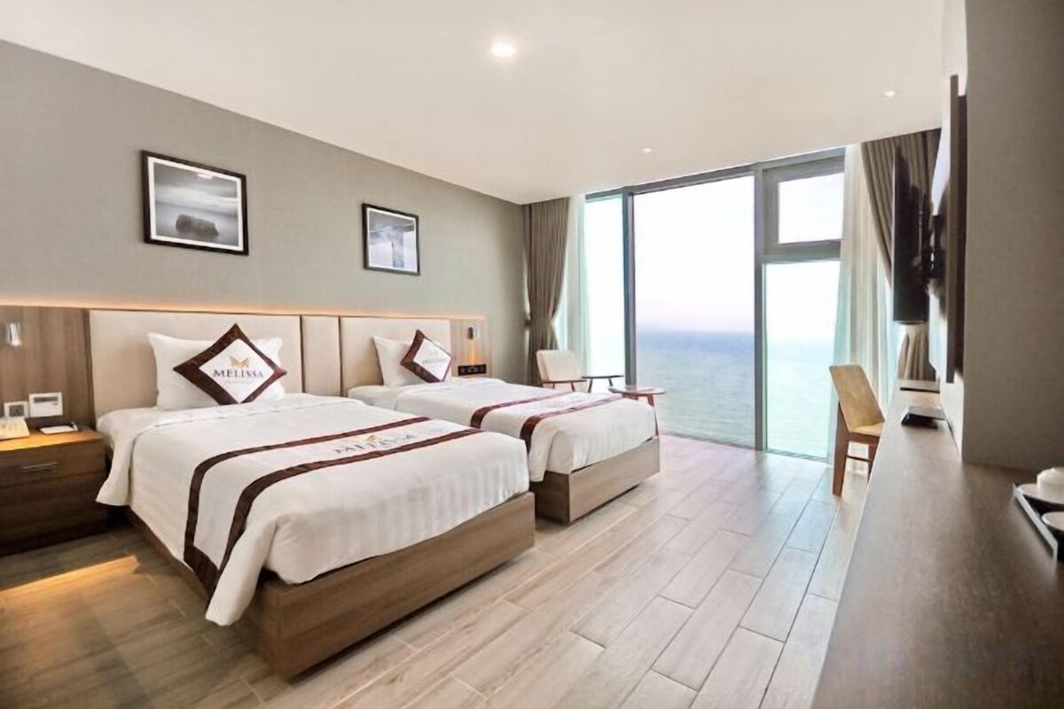 A hotel room with two beds, a large window, and a view of the sea.