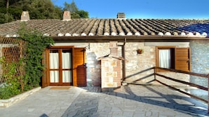 Un bâtiment en pierre avec un toit en tuiles, des portes en bois et un escalier en pierre menant à une terrasse en bois.