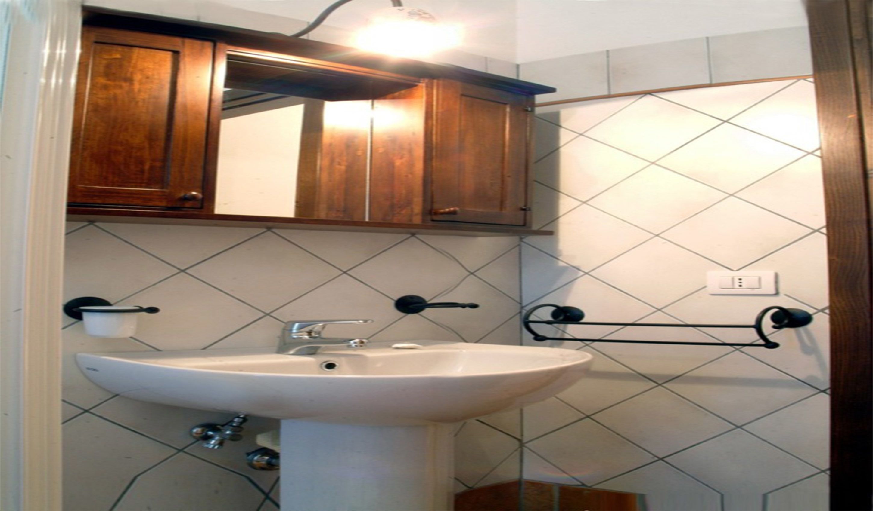 A bathroom with a white sink, wooden cabinets, and a tiled wall.